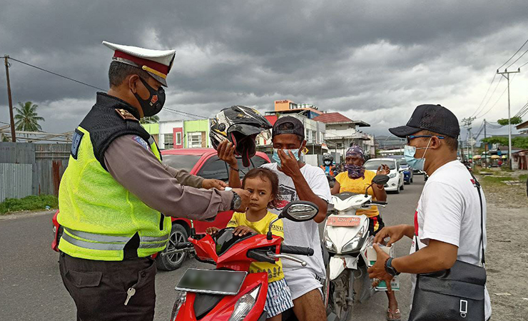 Salah satu wartawan bersama Kasat Lantas Polres Mimika memakaikan masker kepada salah satu pengendara. (Foto: Kristin Rejang/Seputarpapua)