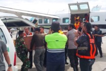 Personel TNI, Polri, petugas maskapai dan keluarga ketika memindahkan peti jenazah Damri dari pesawat ke mobil jenazah saat tiba di Bandara Mozes Kilangin Timika, Selasa (24/1/2023). (Foto: Ist)